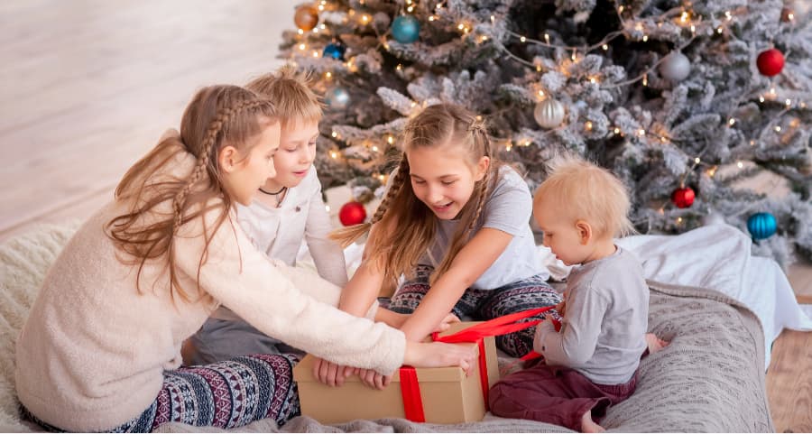 Children opening a gift next to a Christmas tree.